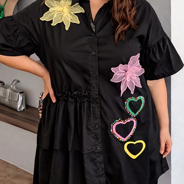 Black dress with colorful floral and heart designs worn by a person indoors.