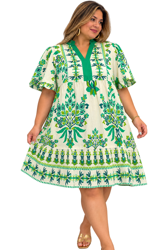 Plus-size model wearing ivory and green botanical print mini dress with flutter sleeves and tiered hem.